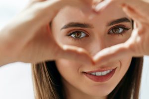femme souriante formant un cœur avec ses mains devant ses yeux aux longs cils