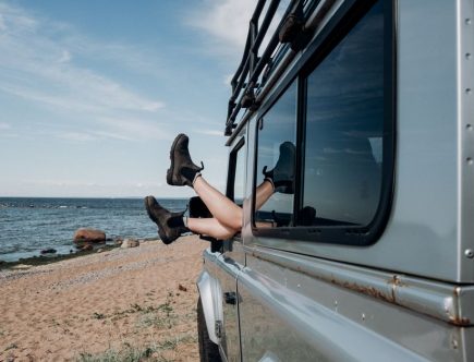 Relaxing beach scene with legs hanging out of car window, showcasing adventure and freedom.
