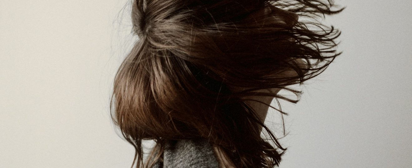 femme de profil avec cheveux longs bruns volant au vent, portant un pull gris
