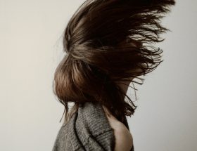 femme de profil avec cheveux longs bruns volant au vent, portant un pull gris