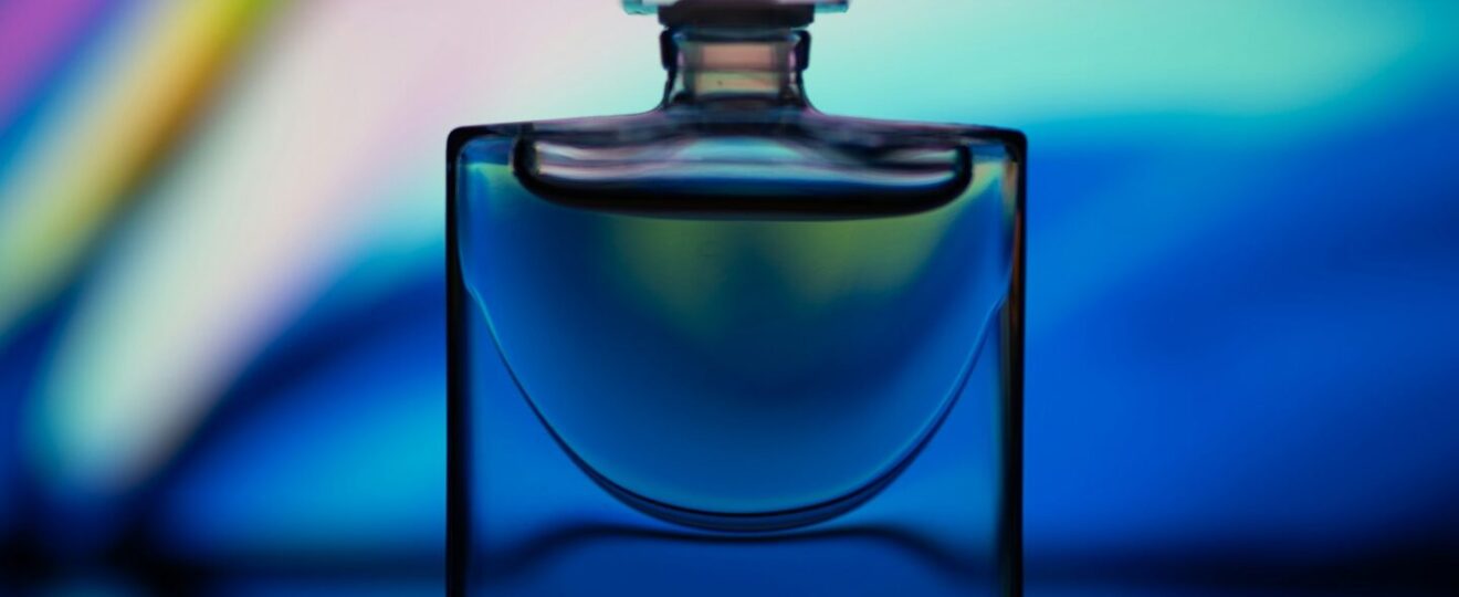 flacon de parfum bleu avec bouchon carré sur fond arc-en-ciel coloré