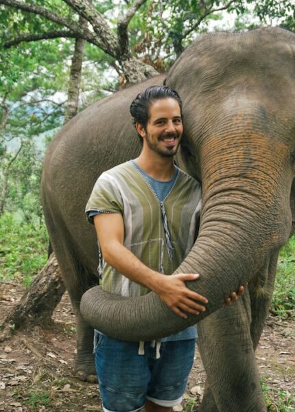 A man standing next to an elephant in a forest